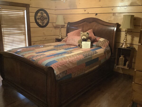 Un dormitorio con paneles de madera, una cama, dos lámparas de noche, un osito de peluche y un cartel sobre la cama.