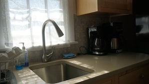 Een keuken met een roestvrijstalen spoelbak, een koffiezetapparaat en een raam met gordijn.