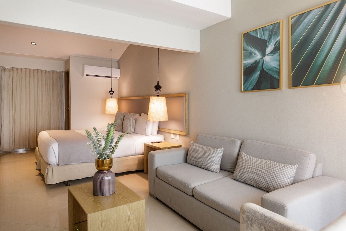 A hotel room with a bed, a sofa, a nightstand, a lamp, and a wall-mounted air conditioner.