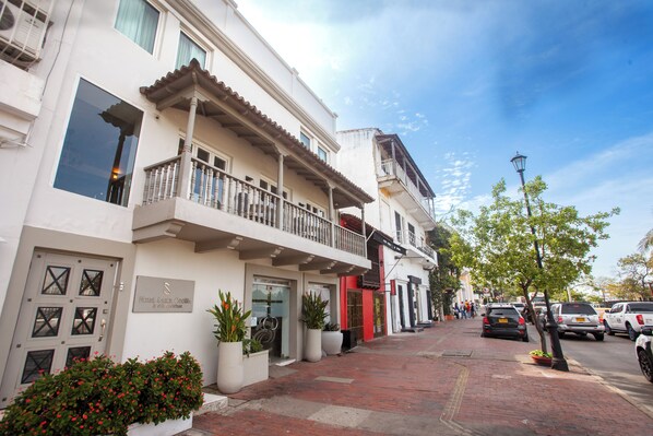 A hotel with a white facade, balconies, and potted plants along the sidewalk.