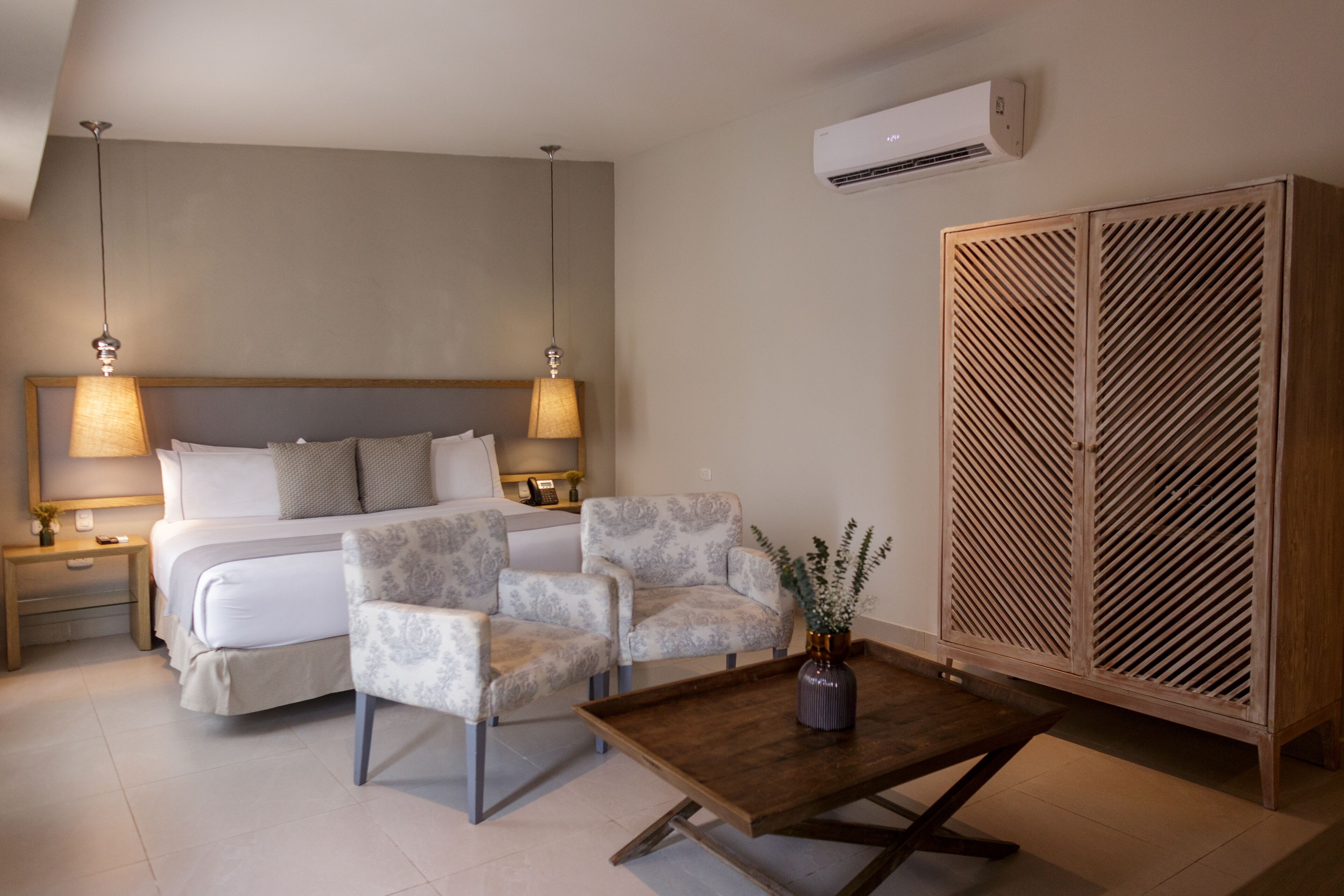 A bedroom with a bed, two nightstands, two lamps, a wooden wardrobe, and a small table with a vase.
