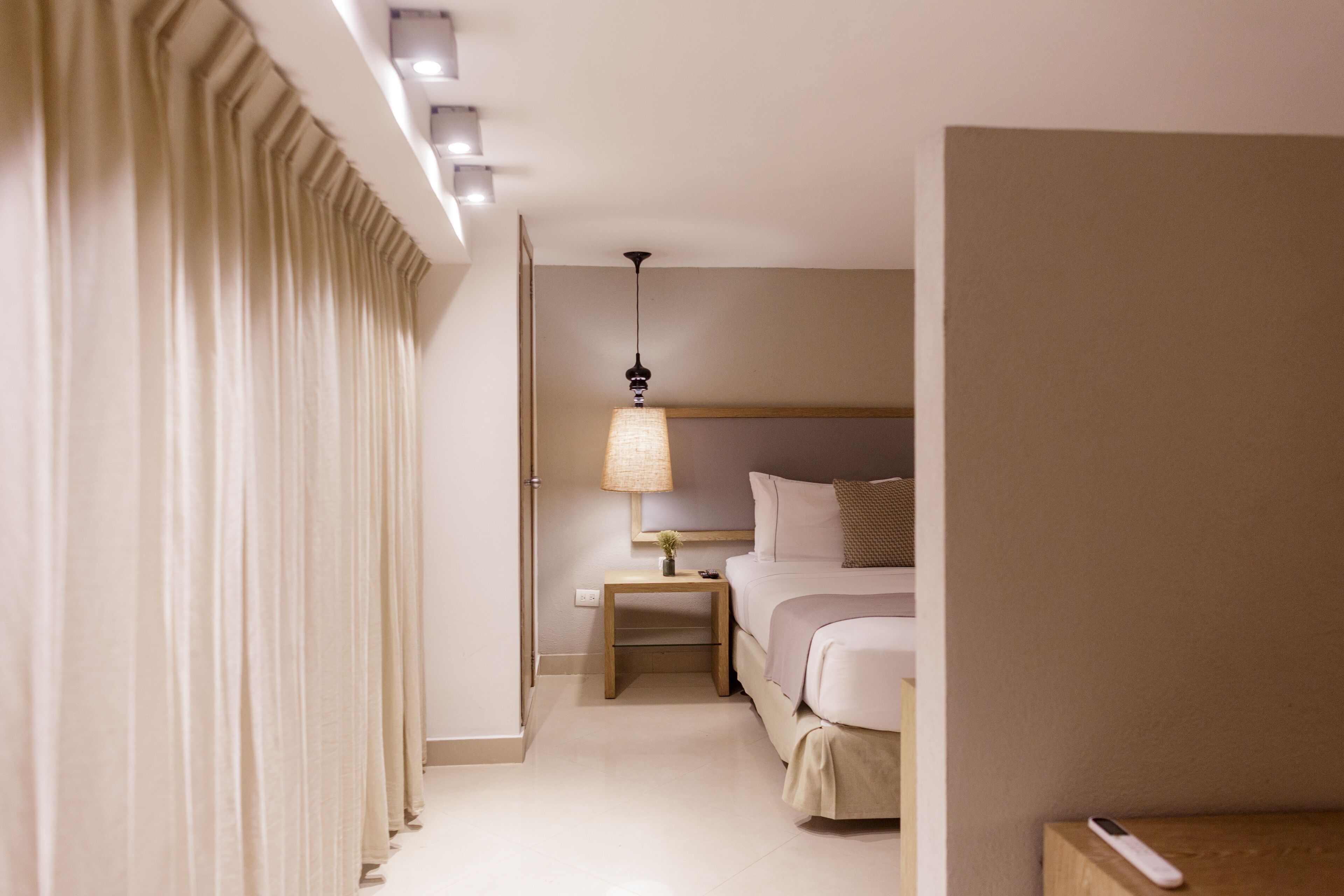 Una camera d'albergo con un letto, comodino, lampada e tende.