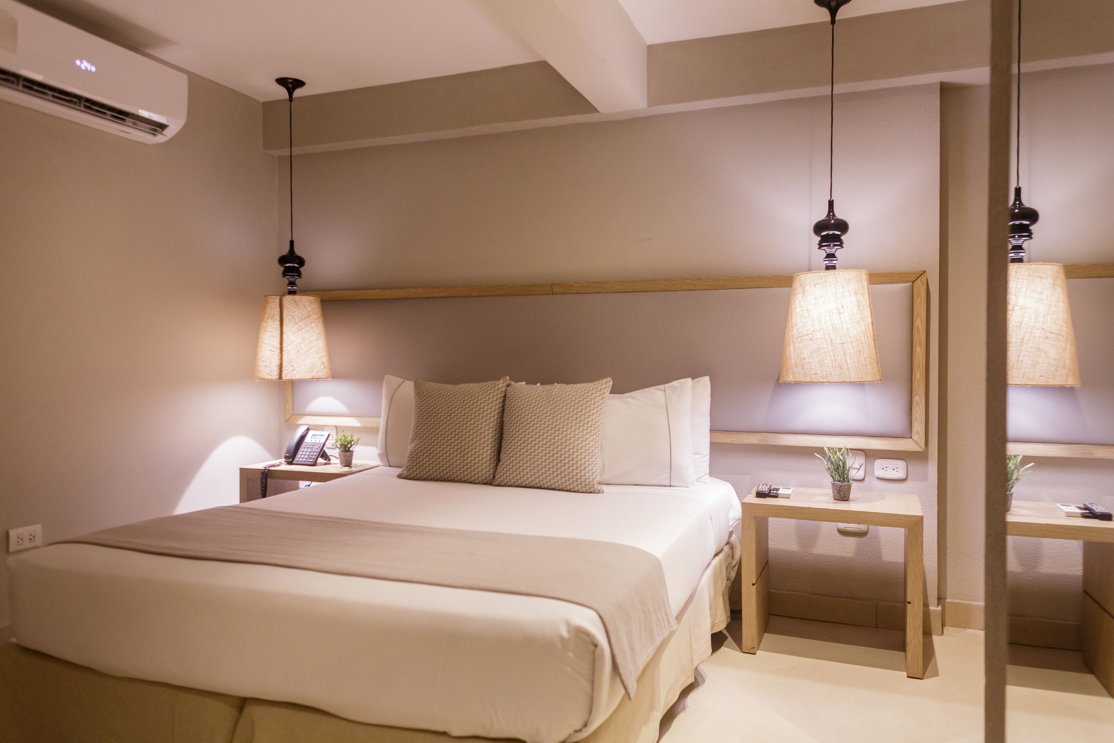 A hotel room with a bed, bedside tables, lamps, and an air conditioning unit.