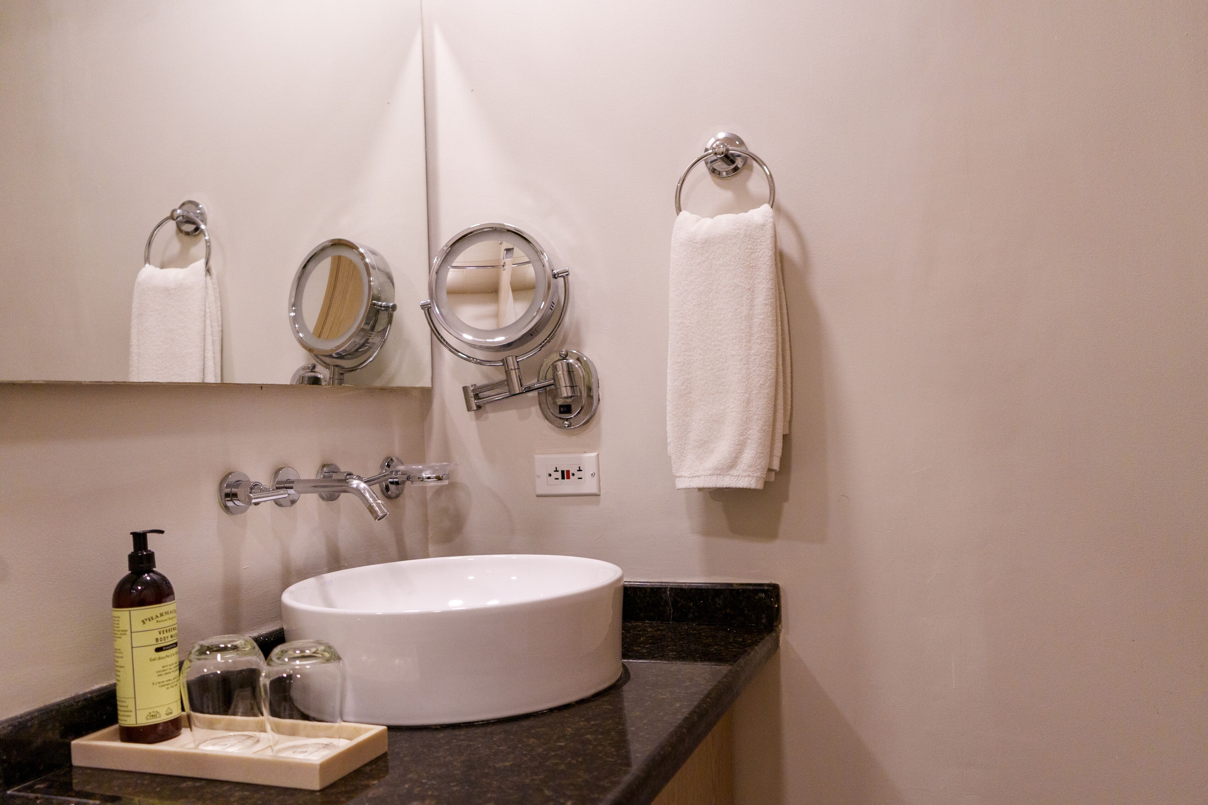 A bathroom with a white sink, two mirrors, a towel rack, and a bottle of shampoo.