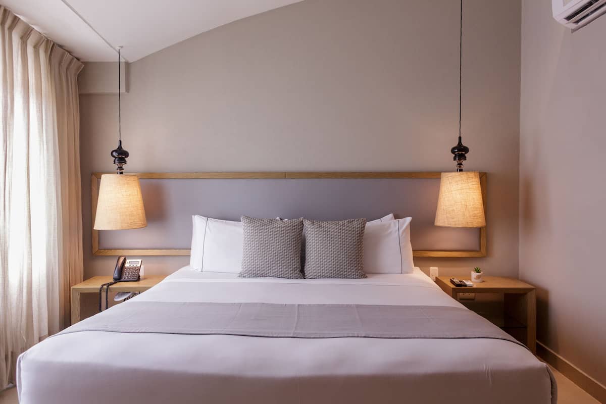 Een net opgemaakt bed met een witte deken en twee kussens, met aan beide kanten nachtkastjes met lampen en een telefoon.