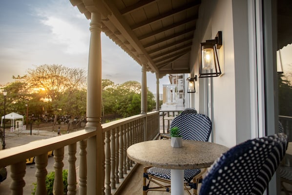 A balcony with a round table and chairs, a potted plant, and a view of trees and a building in the background. - Hotel Santa Cecilia B&B (Cartagena)