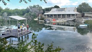 A dock with a covered seating area and a building with a sloped roof in the background. - Top of the Dam Group Campground at Lake Godstone (Graford)