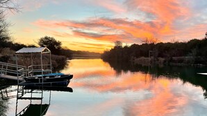 A calm river with boats docked at a pier, surrounded by trees and a clear sky. - Top of the Dam Group Campground at Lake Godstone (Graford)