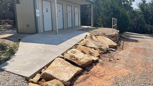 A building with a covered outdoor area, multiple doors, and a concrete pathway leading to it. - Top of the Dam Group Campground at Lake Godstone (Graford)