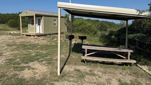 A small, single-story building with a door and window, a picnic table, and a covered area with a bench. - Top of the Dam Group Campground at Lake Godstone (Graford)