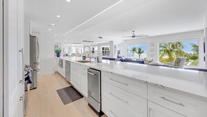 A modern kitchen with white cabinetry, a large island, and a view of palm trees. - Sublime Sunsets at the Truman Annex in Key West (Key West)