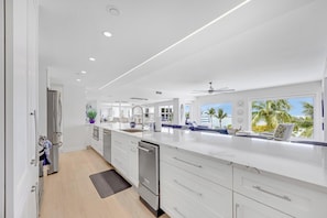 A modern kitchen with white cabinetry, a large island, and a view of palm trees.