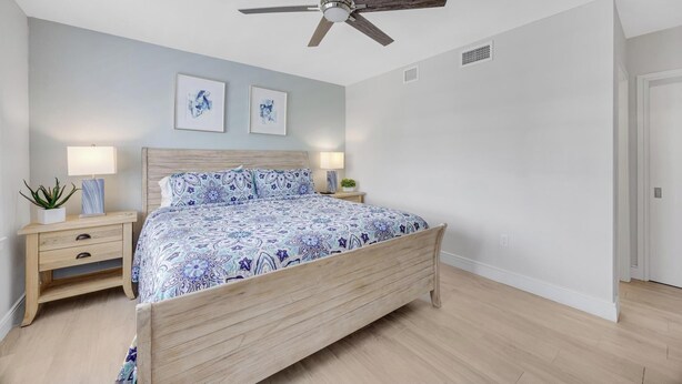 A bedroom with a wooden bed, a ceiling fan, two wall-mounted lamps, and two framed artworks. - Sublime Sunsets at the Truman Annex in Key West (Key West)