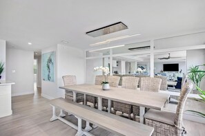 A modern dining area with a long table, wicker chairs, and a bench.