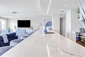 Uma sala de estar moderna com um balcão de mármore extenso, uma TV de tela plana, um sofá e uma cozinha com armários e fogão.