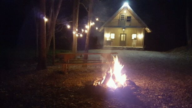 Puinen penkki ja nuotiopaikka metsäisellä alueella, taustalla näkyy talo.