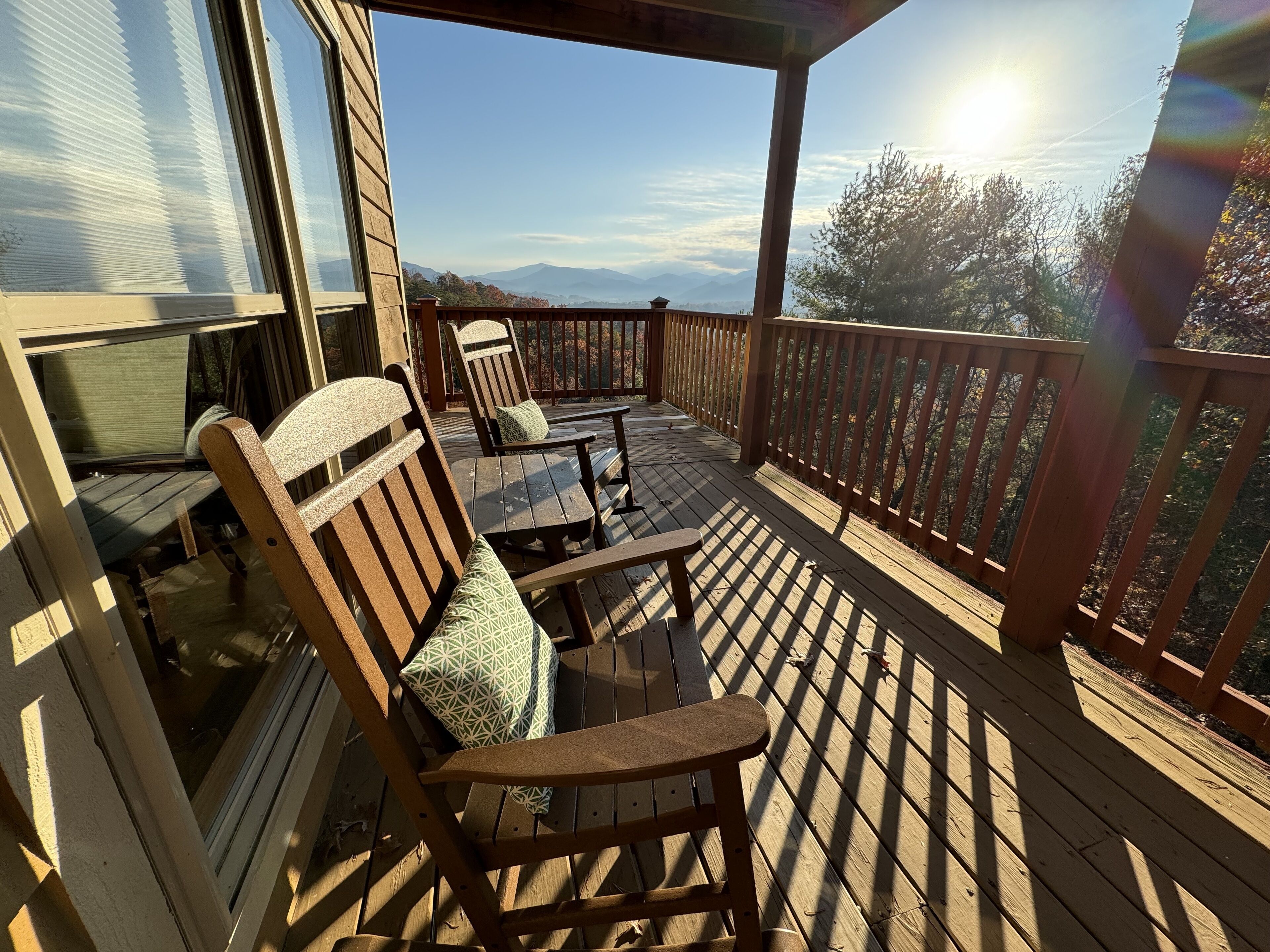 A wooden deck with two chairs and a table, overlooking a mountainous landscape.