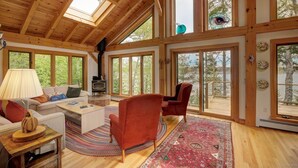 Un salon spacieux doté d’un plafond en bois, de grandes fenêtres, d’une cheminée et d’un coin salon confortable.