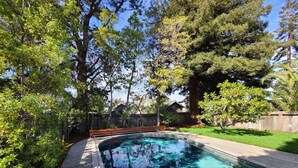 A clear swimming pool surrounded by trees and a wooden fence. - Coastal Zen Den (Alameda)