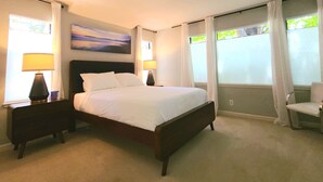 A neatly arranged bedroom with a large bed, two bedside lamps, a chair, and a painting on the wall. - Coastal Zen Den (Alameda)
