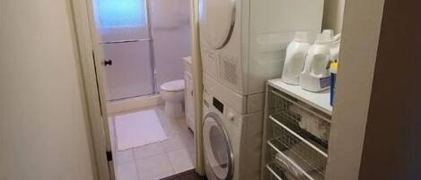 A laundry room with a washing machine, dryer, and shelves with detergent bottles.