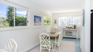 A dining area with a table and chairs, framed pictures on the wall, and a view of trees through the windows.
