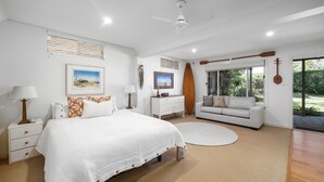 A bedroom with a bed, bedside tables, a dresser, a sofa, and a large window with a view of greenery.
