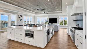 Un'ampia cucina con una grande isola, mobili bianchi e una moderna ventola a soffitto.