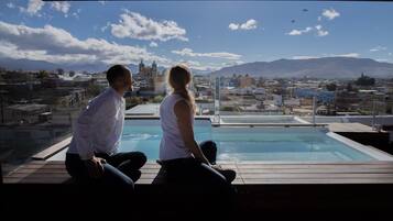 A couple sitting by a pool with a cityscape and mountains in the background.