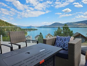 A balcony with wicker furniture, a table, and a view of a lake and mountains.