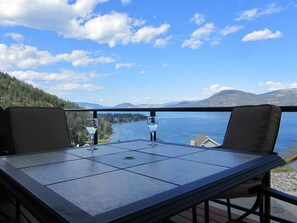 A table with two chairs and two wine glasses, overlooking a lake and mountains.