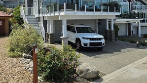 A modern two-story house with a large garage, a covered outdoor seating area, and a driveway with a parked SUV. - FULLY RENOVATED LAKEVIEW COTTAGE / PET FRIENDLY - LA CASA (Kelowna)