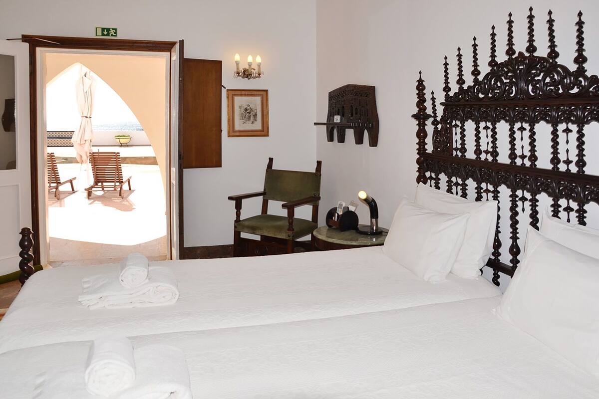 Habitación de hotel con cama, una silla, una mesita con lámpara y un adorno en la pared.