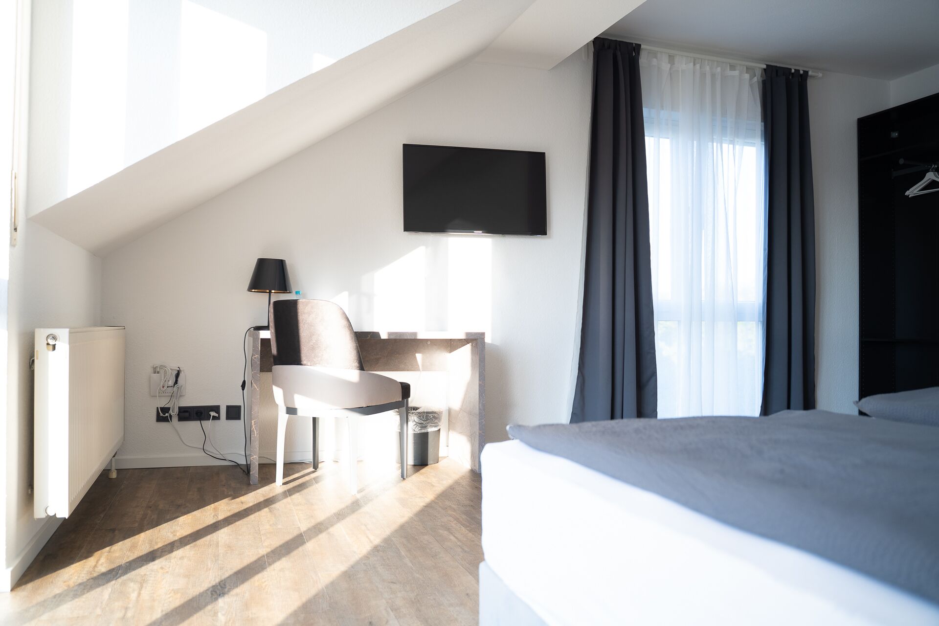 Un dormitorio con cama, escritorio, silla y televisor en la pared.