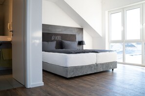 A modern bedroom with a large bed, a headboard with the text "AP HOTEL", a window with a view, and a wooden floor. - AP Hotel Mannheim Viernheim (Viernheim)