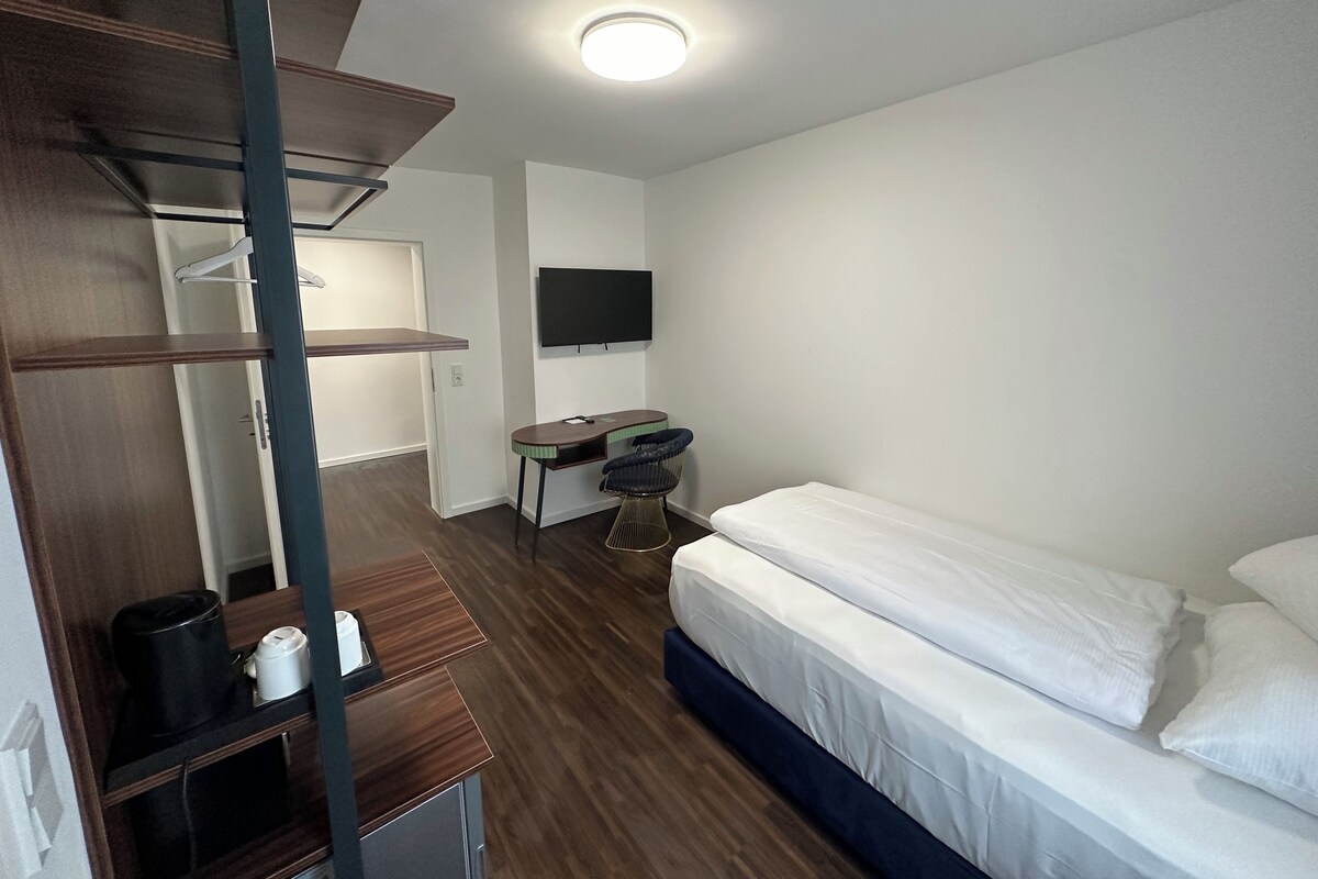 A hotel room with a bed, a desk, a chair, a TV, and a wardrobe.