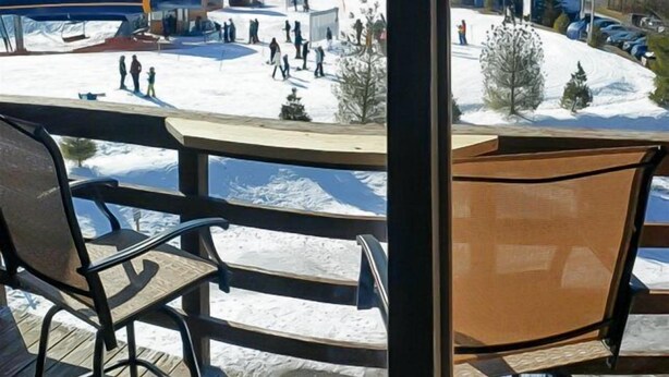 Blick vom Balkon mit Holzboden und Metallstühlen auf eine verschneite Landschaft mit Seilbahn und Personen.