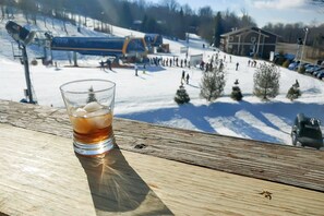 A glass of iced beverage on a wooden surface with a ski resort in the background. - Herzwoods C303 (Davis)