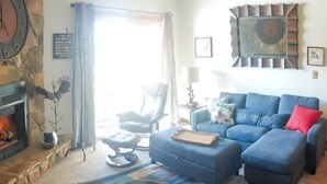 Ein Wohnzimmer mit Kamin, einem blauen Sofa, einem Sessel und einem Teppich.