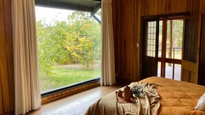 Una habitació de fusta amb un finestral gran, un llit amb llençol beix i una làmpada penjant.