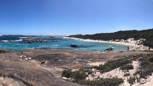 Paisatge costaner amb terreny rocos, una platja sorrenca i l'oceà.