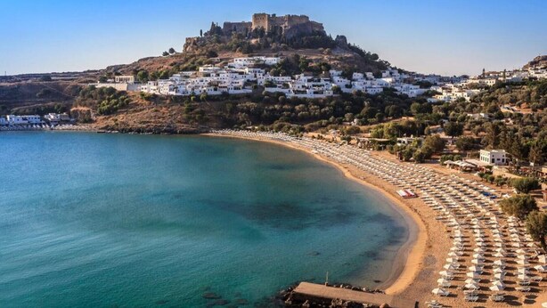 A coastal town with a castle on a hill, a beach with umbrellas, and white buildings. - Anssami Villa  (Rhodes)