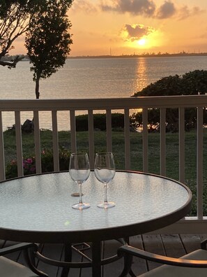 A round table with two wine glasses on a balcony overlooking a sunset over a body of water.
