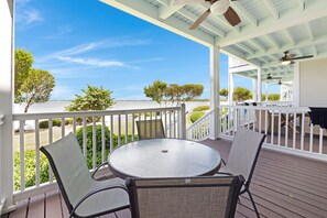 A covered outdoor area with a round table and chairs, a white railing, and a view of the ocean.