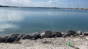 Una spiaggia con mare calmo, un litorale roccioso e un molo in lontananza.