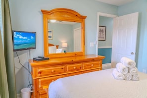 A hotel room with a large bed, a wooden dresser, a television, and a door.