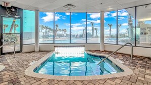 Área de piscina com vista desobstruída para palmeiras e um céu azul através de amplas janelas.