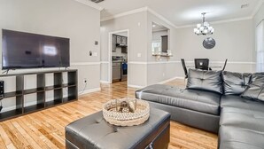Uma sala de estar moderna com televisão de tela plana, sofá de couro e piso de madeira.
