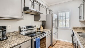 Cozinha moderna com eletrodomésticos de aço inoxidável, bancadas de granito e armários brancos.