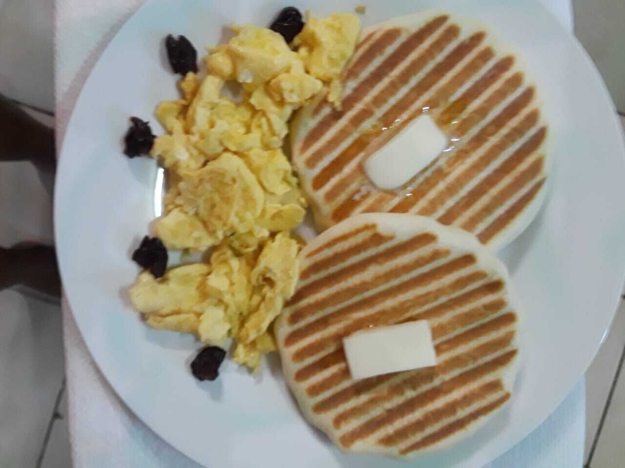A plate with scrambled eggs, two pancakes with butter, and raisins.